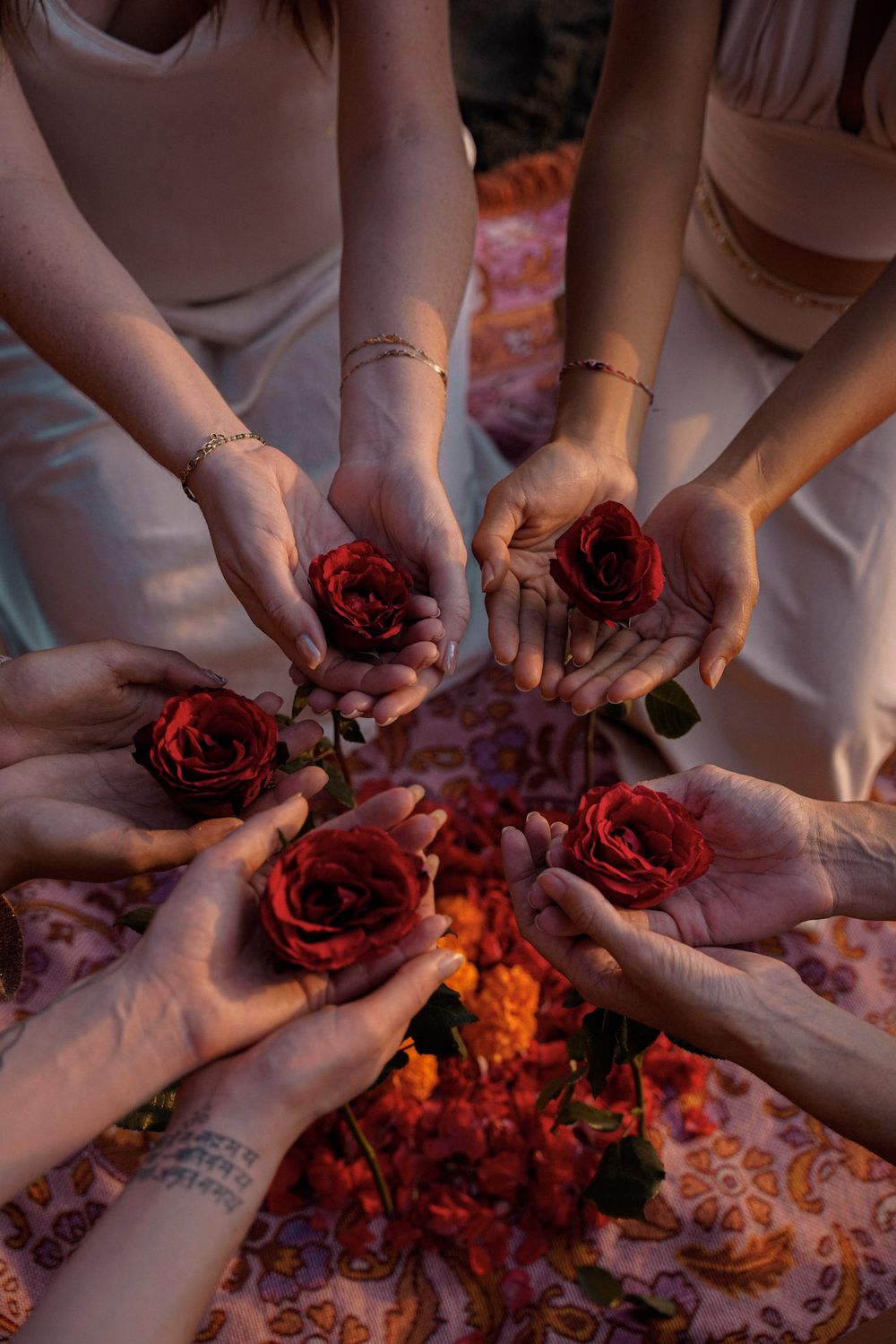 A circle of women's hands, each holding a red rose over a carpet of petals